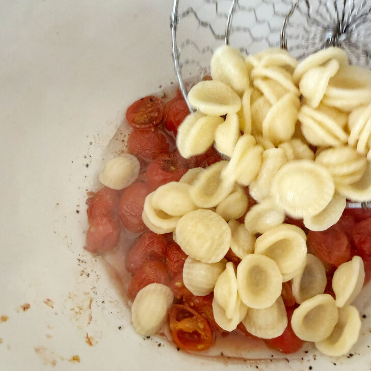 Cooked orecchiette being added to roasted tomato mixture.