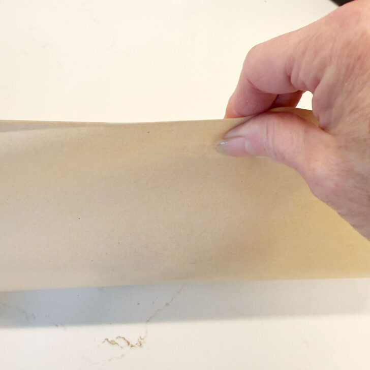 Pulling the two ends of the parchment together over the top of the sandwich.