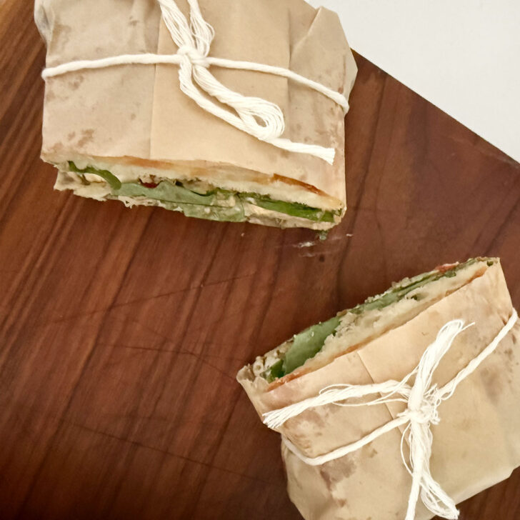 Parchment-wrapped focaccia sandwiches cut in half.