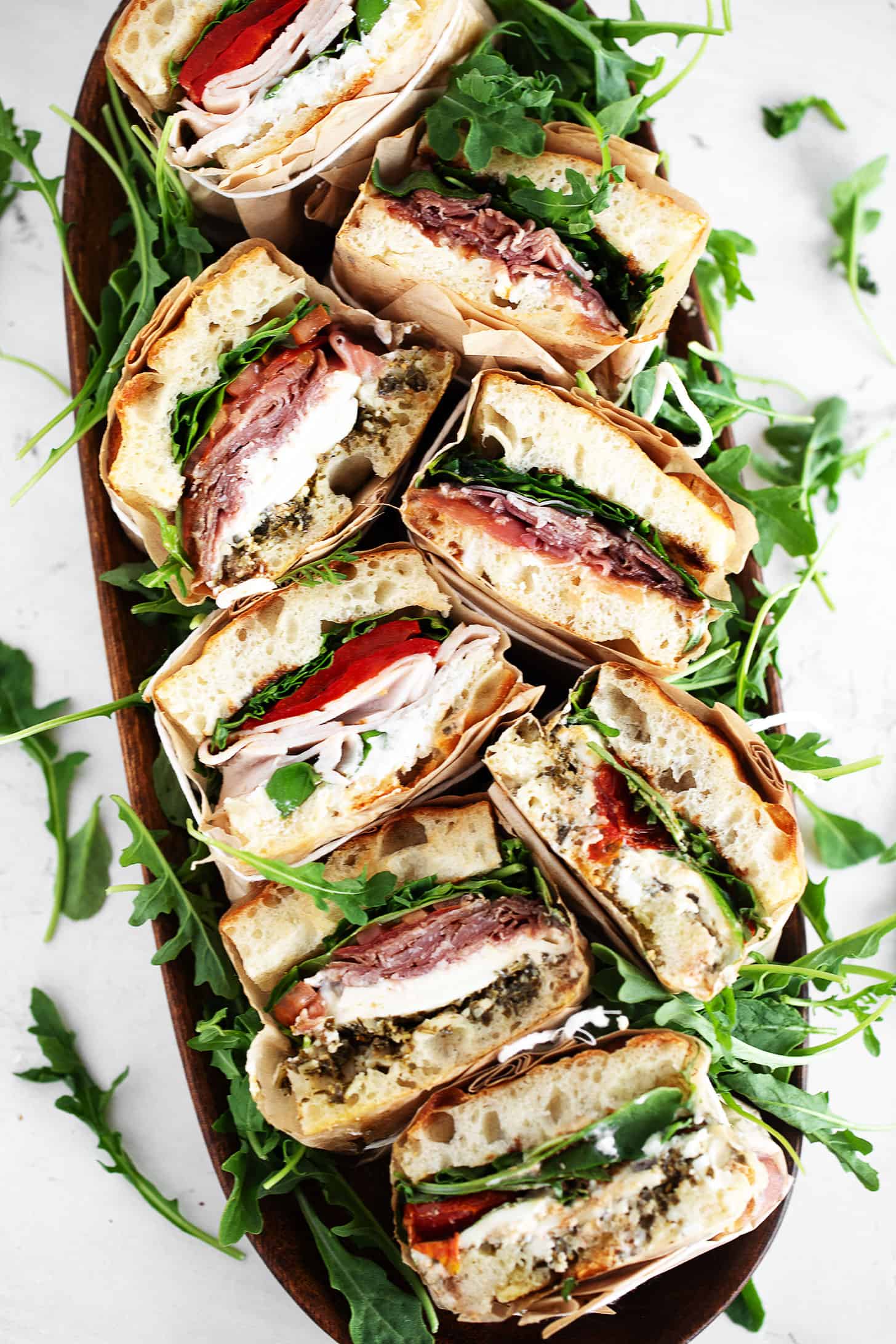 Focaccia sandwiches wrapped in parchment and cut in half on a serving platter.