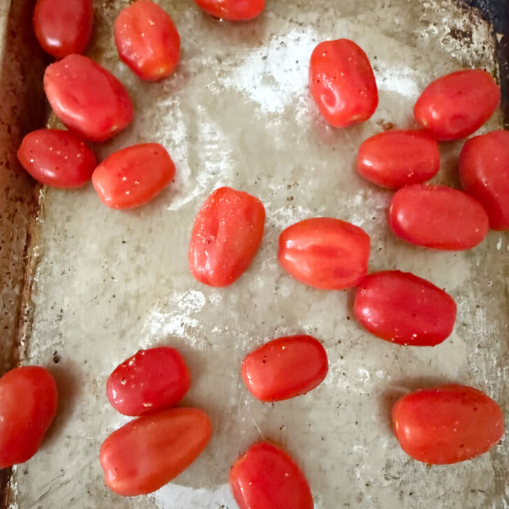 Cherry tomatoes are scattered on a baking sheet before roasting.