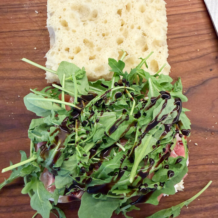 Arugula added to the top of the sandwich with balsamic glaze and olive oil.
