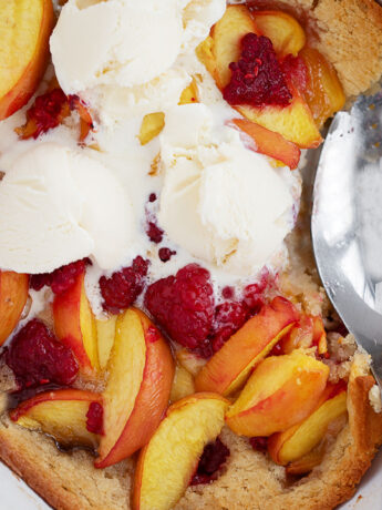 Peach melba spoon cake in the baking dish with a spoon.