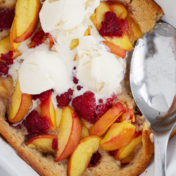 Peach melba spoon cake in the baking dish with a spoon.