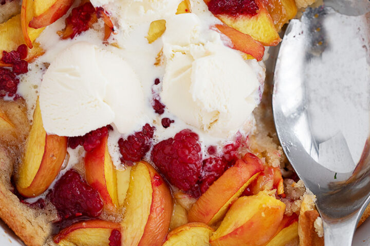 Peach melba spoon cake in the baking dish with a spoon.