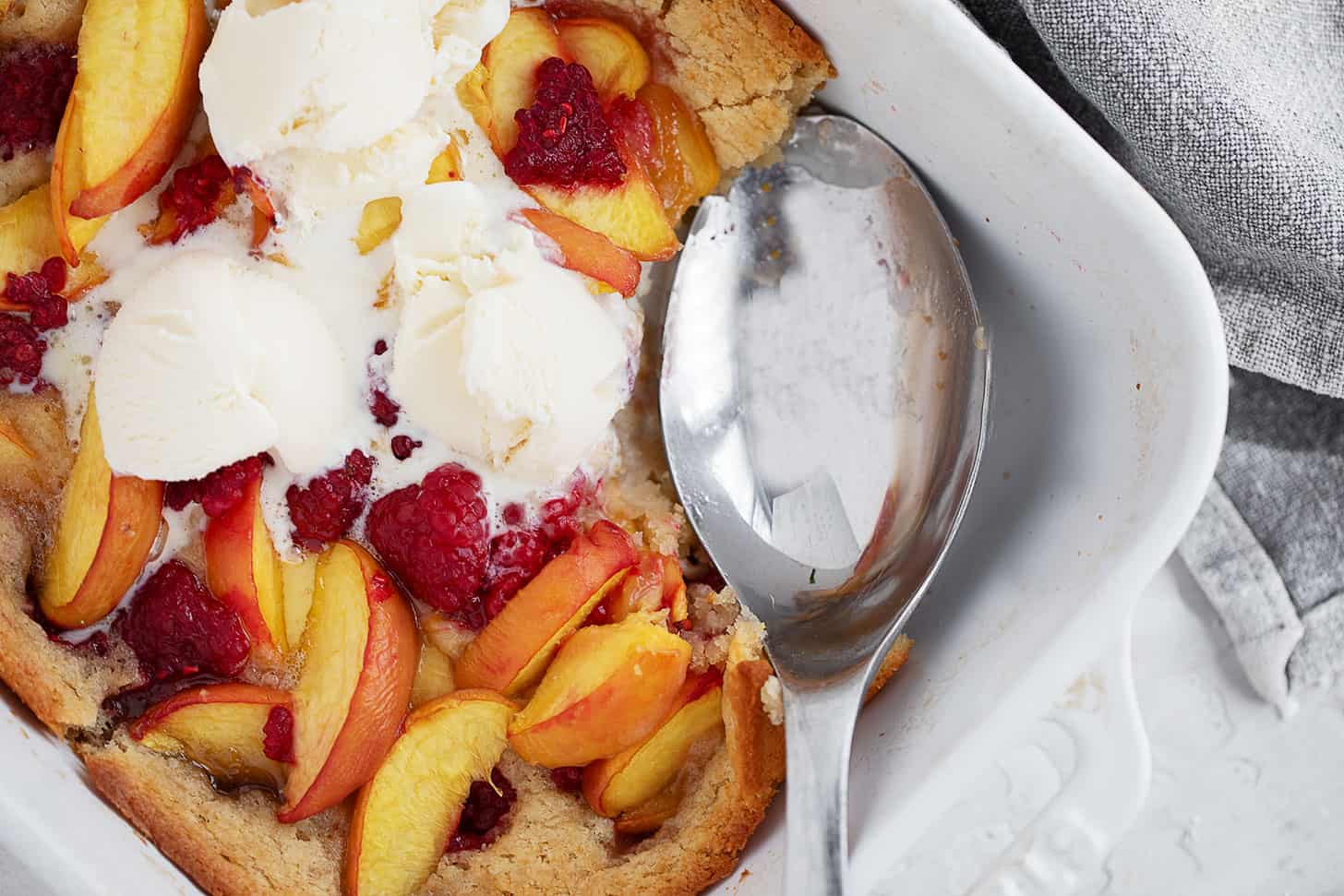 Peach melba spoon cake in the baking dish with a spoon.