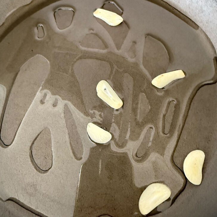 Heating garlic slices in oil in a skillet.