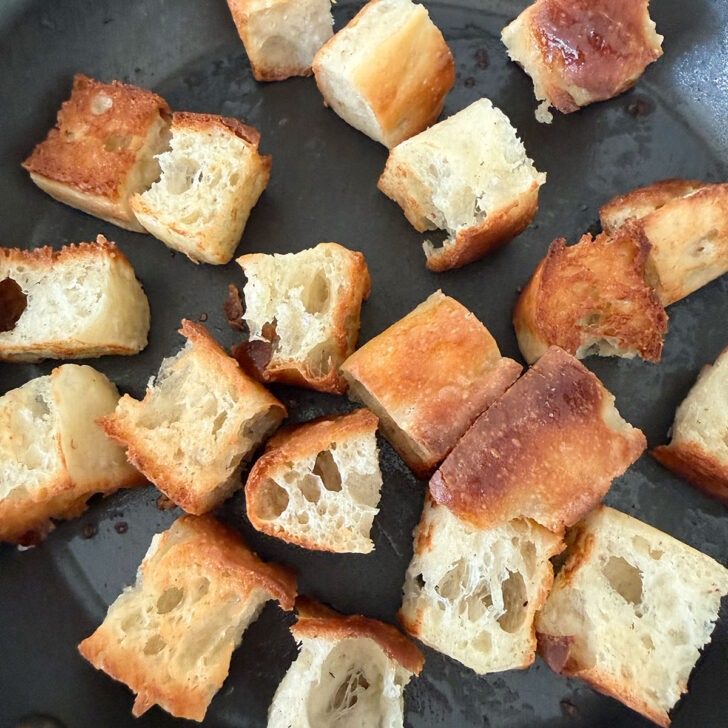 Focaccia cubes added to the hot garlic oil in the skillet to fry.