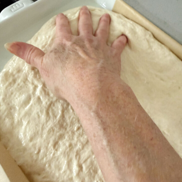 Stretching the focaccia dough into the pan.