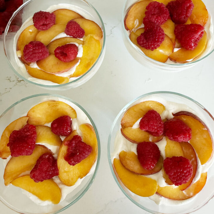 Adding fresh peaches and raspberries to the dessert cups.