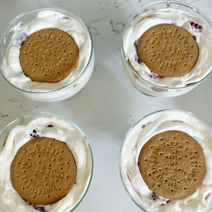 Adding more cream and biscuits to the dessert cups.