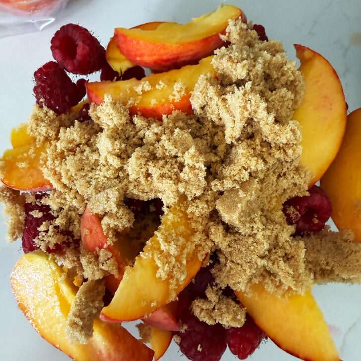 Peaches and raspberries in a bowl with brown sugar.