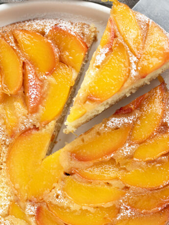 Peach upside-down cake on a serving plate with a slice on a server.