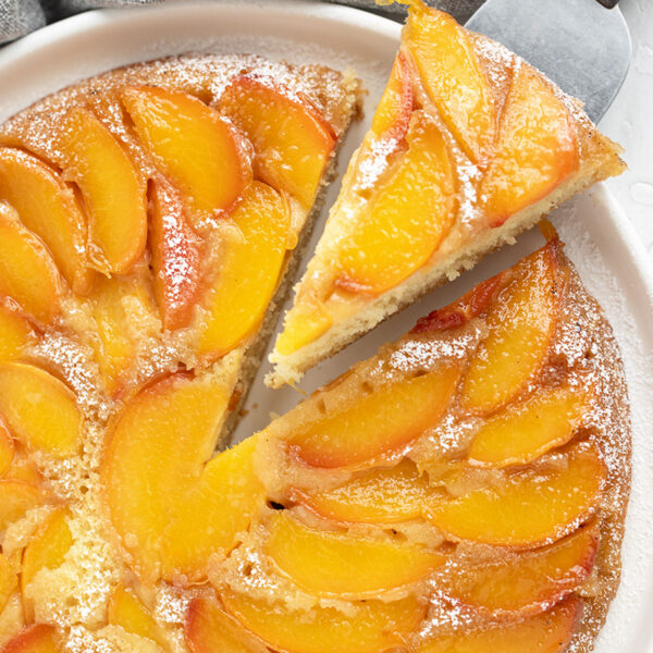 Peach upside-down cake on a serving plate with a slice on a server.