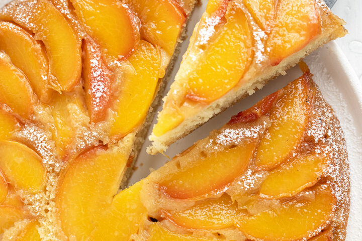 Peach upside-down cake on a serving plate with a slice on a server.