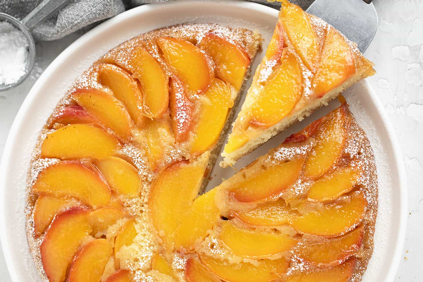 Peach upside-down cake on a serving plate with a slice on a server.