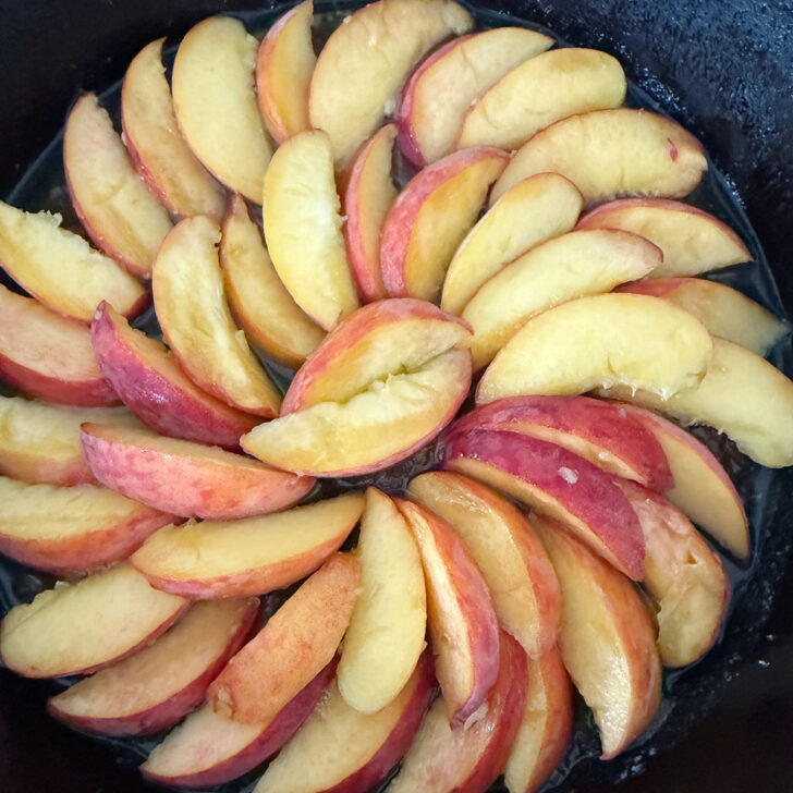 Peach slices arranged over the butter and brown sugar in the skillet.