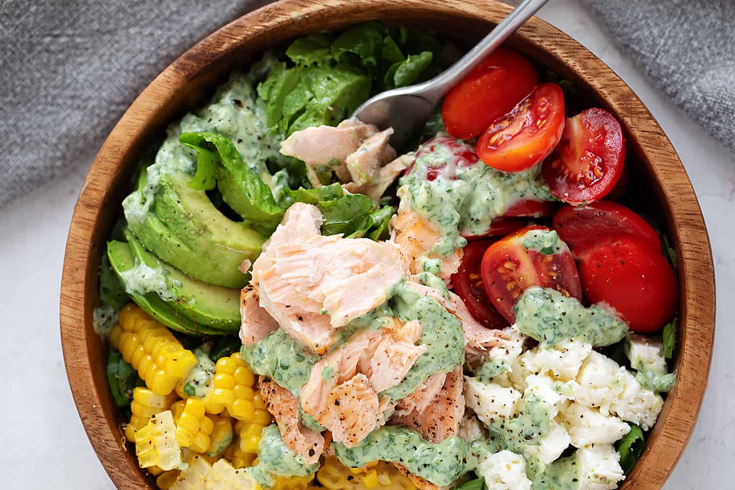 Cilantro lime salmon salad with corn, feta and cherry tomatoes in a wooden salad bowl.