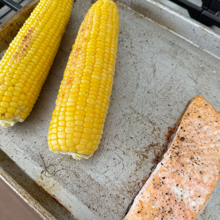 Corn cobs and salmon on a baking sheet after roasting.