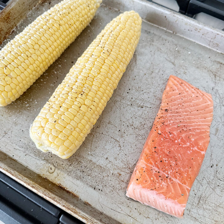 Corn cobs and salmon on a baking sheet before roasting.