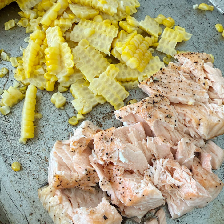 Cooked orn kernels removed from the cob and cooked salmon flaked on a baking sheet.