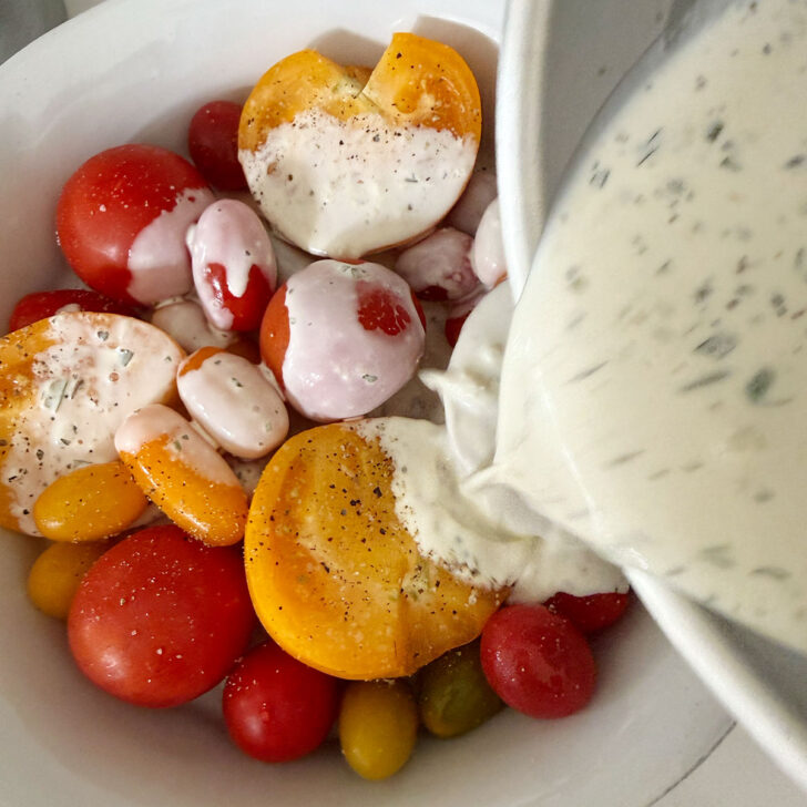 Pouring the infused cream over the fresh tomatoes in the baking dish.