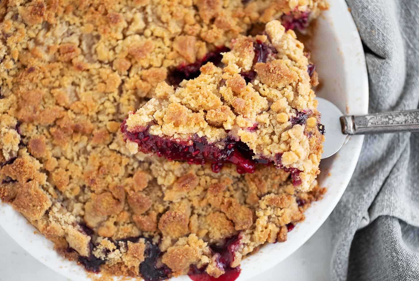 Berry apple crumb pie with a slice on a server.