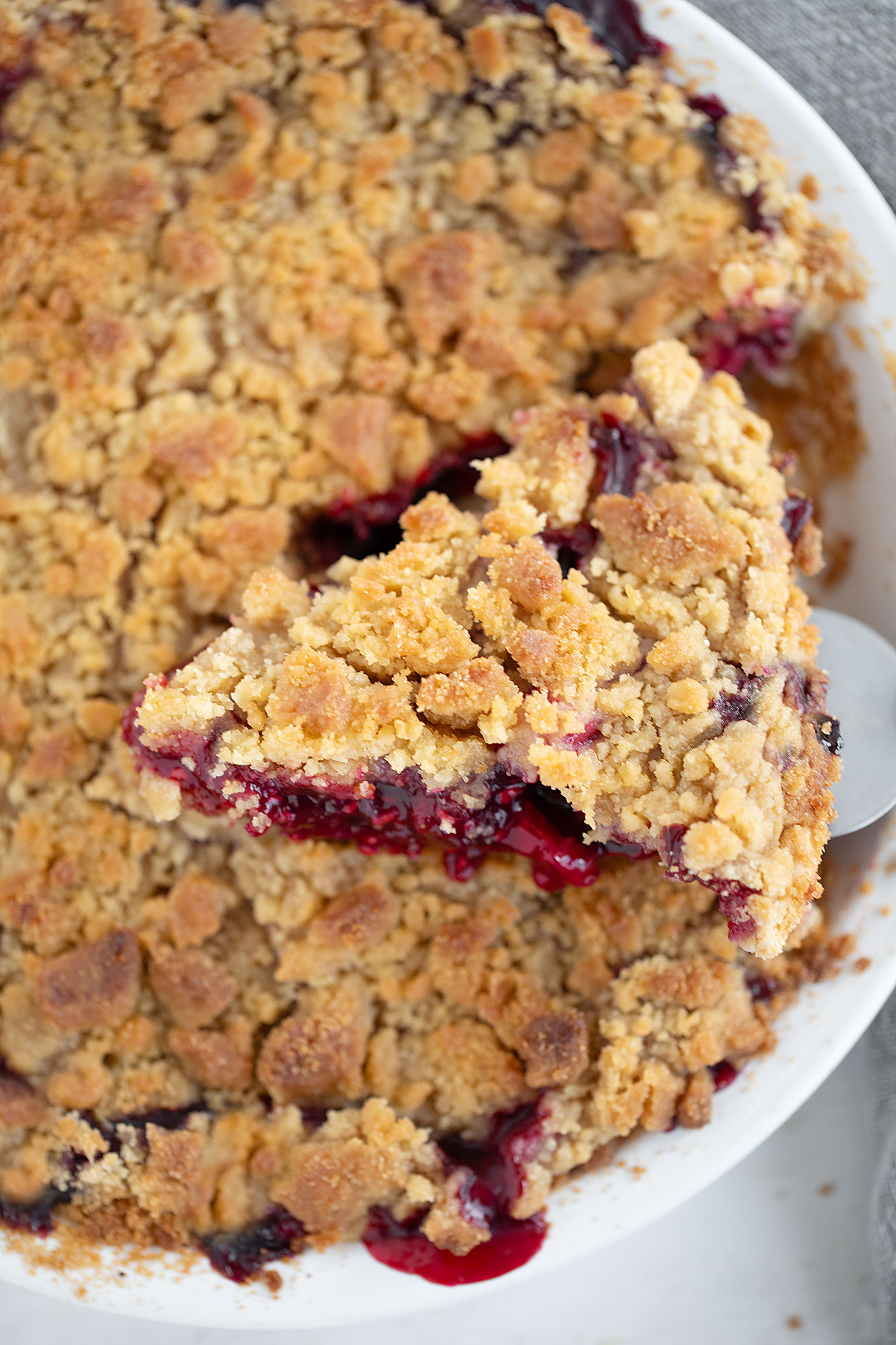 Berry apple crumb pie with a slice on a server.