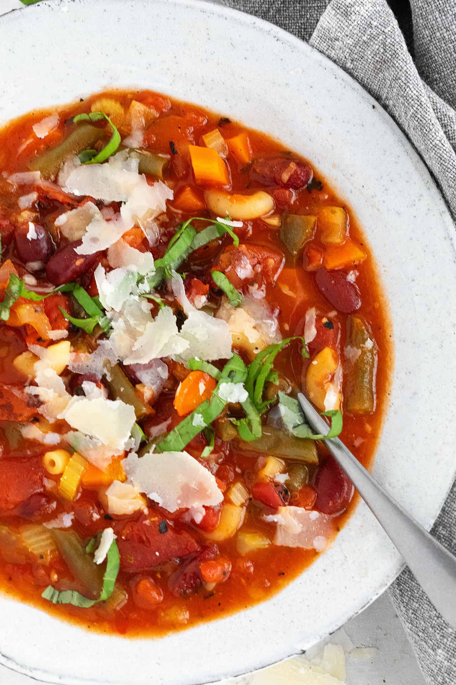 Classic minestrone in a bowl topped with shaved Parmesan and basil leaves.