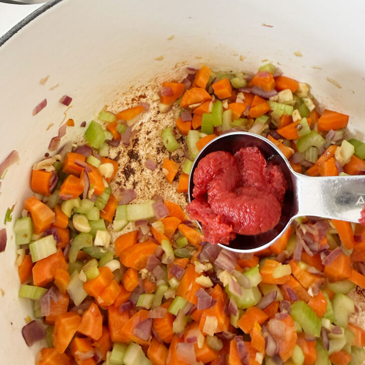 Adding tomato paste to the softened vegetables.