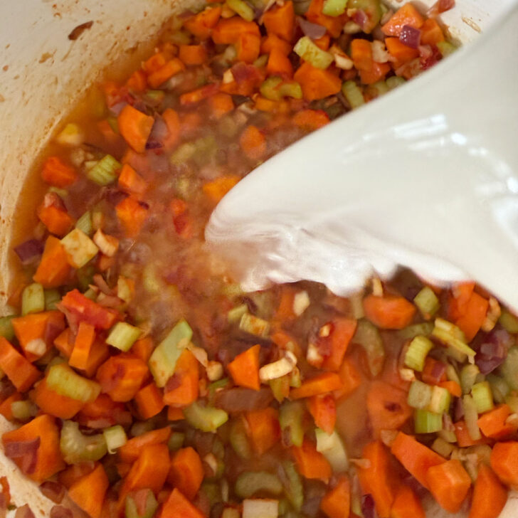 Adding broth to the softened vegetables.
