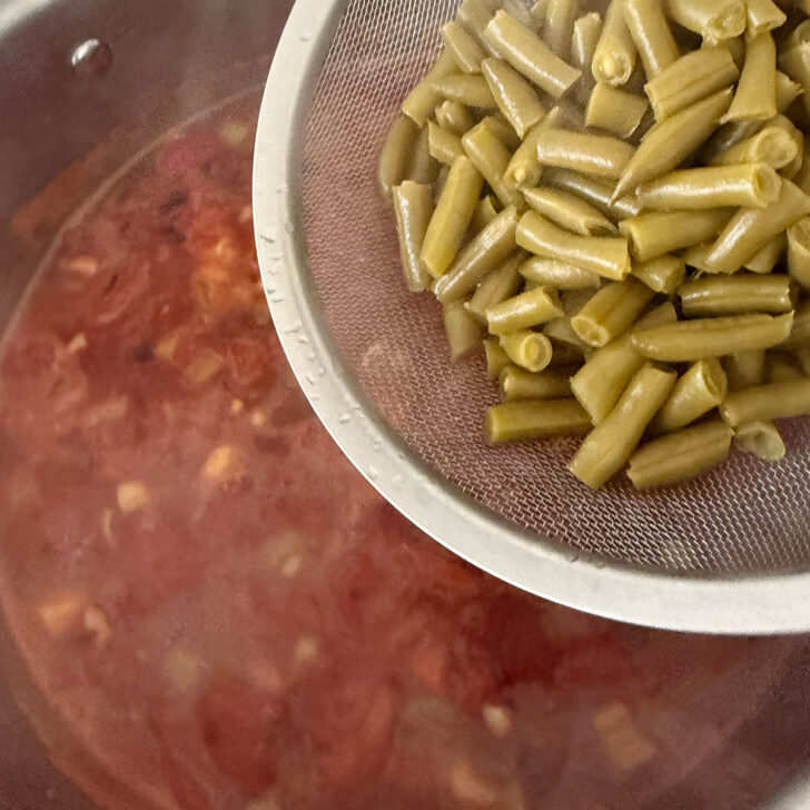 Adding the canned green beans to the pot.