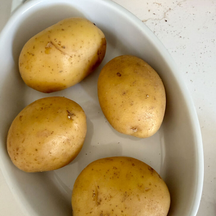 Four whole potatoes in a casserole dish.