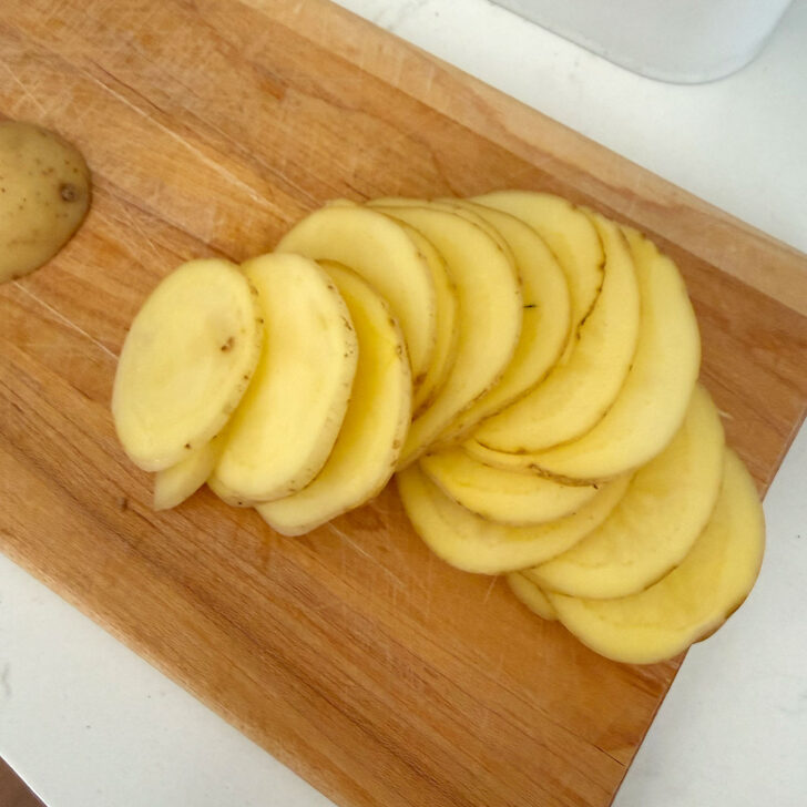 Potatoes thinly sliced on a cutting board.