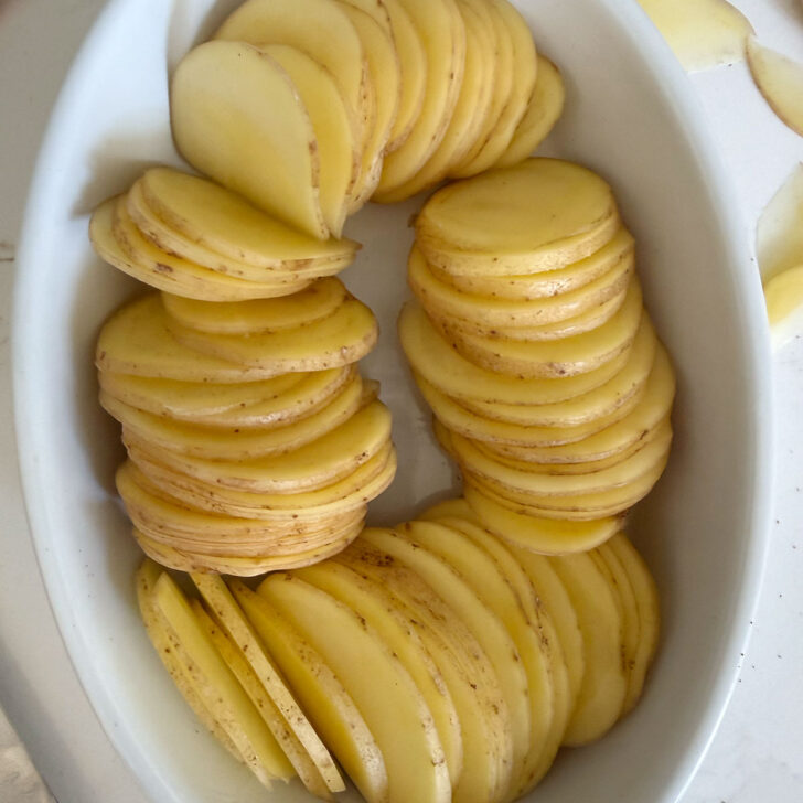 Sliced potatoes arranged in a small casserole dish.