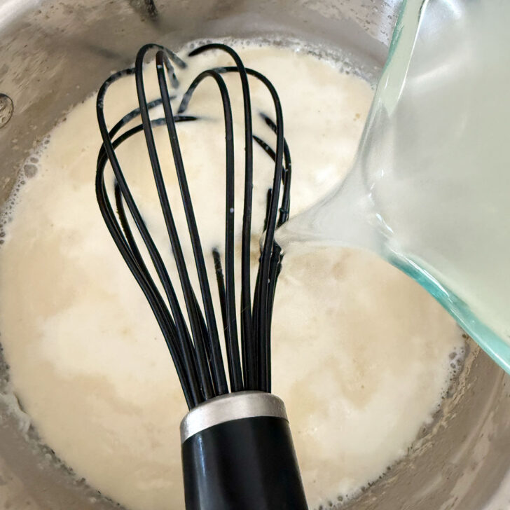Adding chicken broth to the cream sauce.