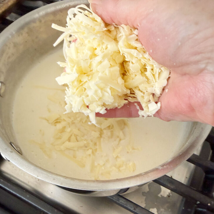 Adding shredded Gruyere cheese to the cream sauce.