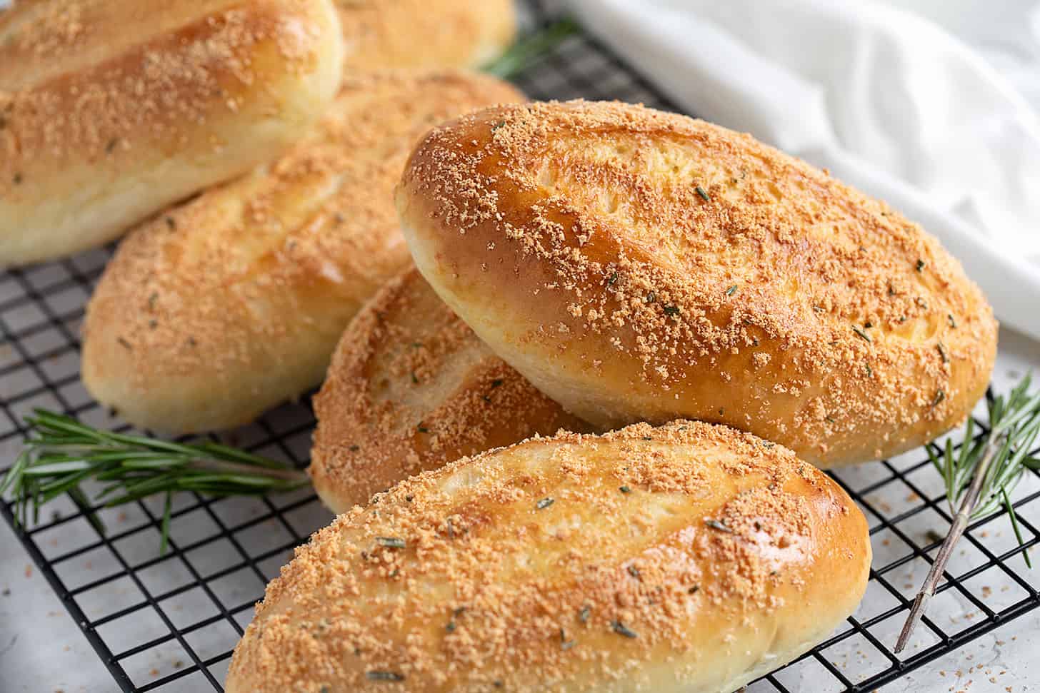 Rosemary Parmesan sandwich buns on a wire cooling rack.