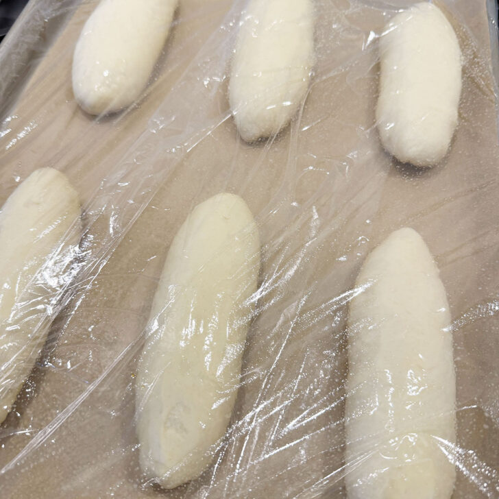 Shaped buns set to rise on the baking sheet covered with plastic wrap.
