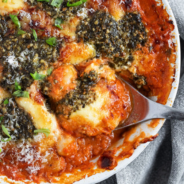 Cherry tomato and pesto baked gnocchi in the baking dish with a spoon.
