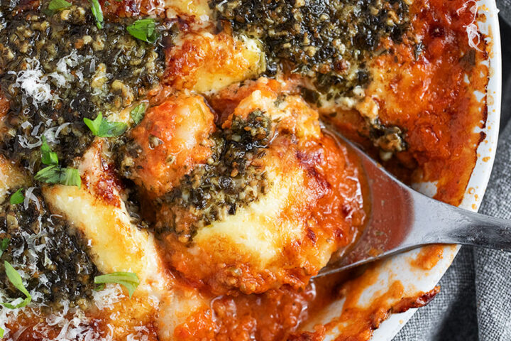 Cherry tomato and pesto baked gnocchi in the baking dish with a spoon.
