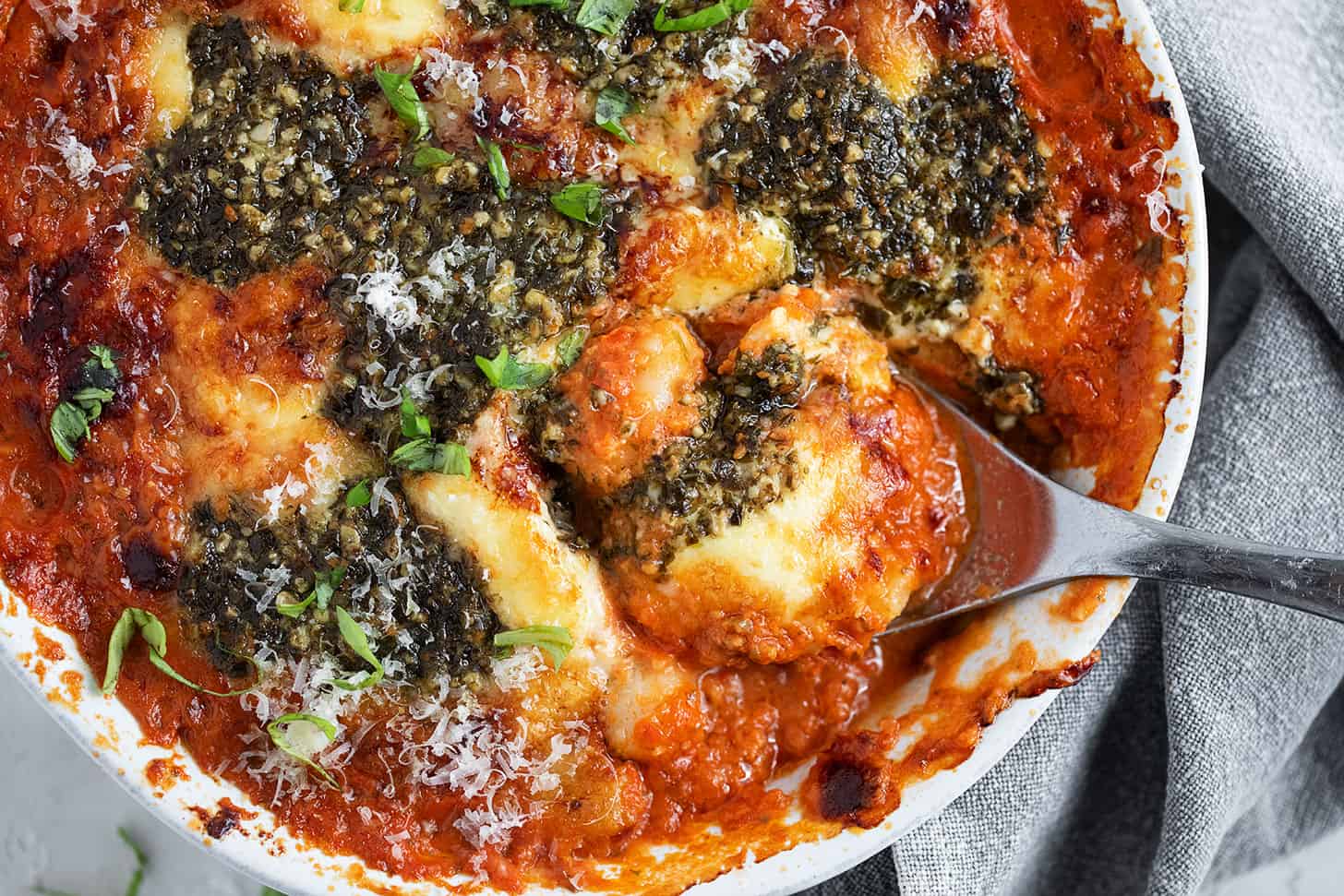 Cherry tomato and pesto baked gnocchi in the baking dish with a spoon.