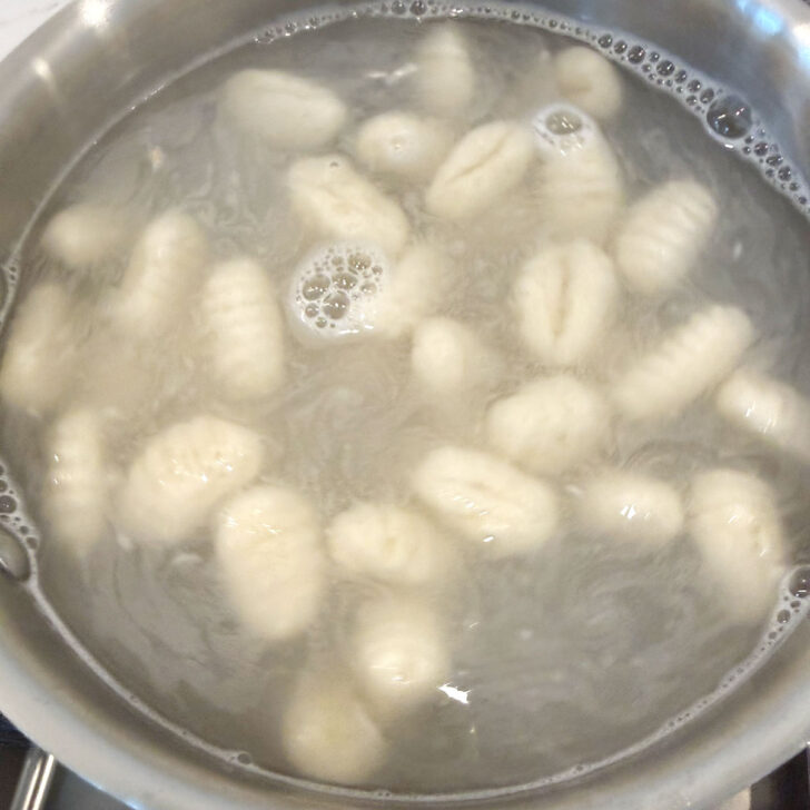 Gnocchi floating in a pot of boiling water.