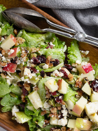 Chopped apple salad in a wooden bowl with silver tongs.