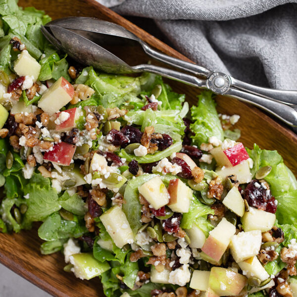 Chopped apple salad in a wooden bowl with silver tongs.