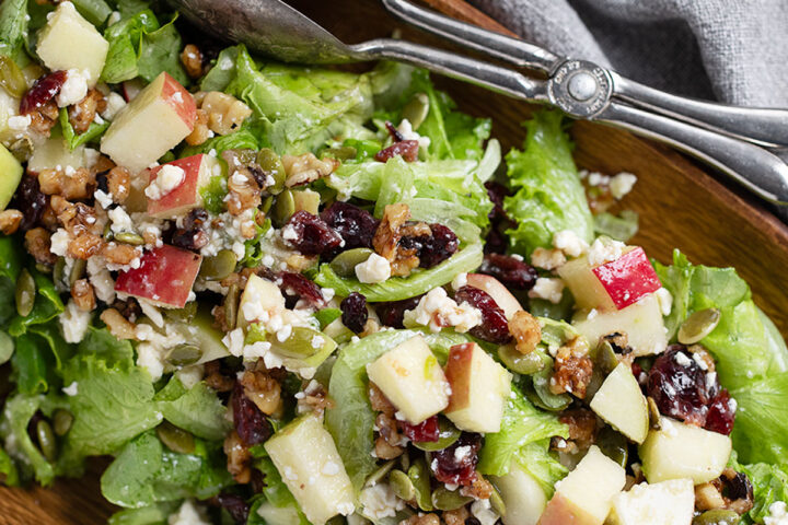 Chopped apple salad in a wooden bowl with silver tongs.