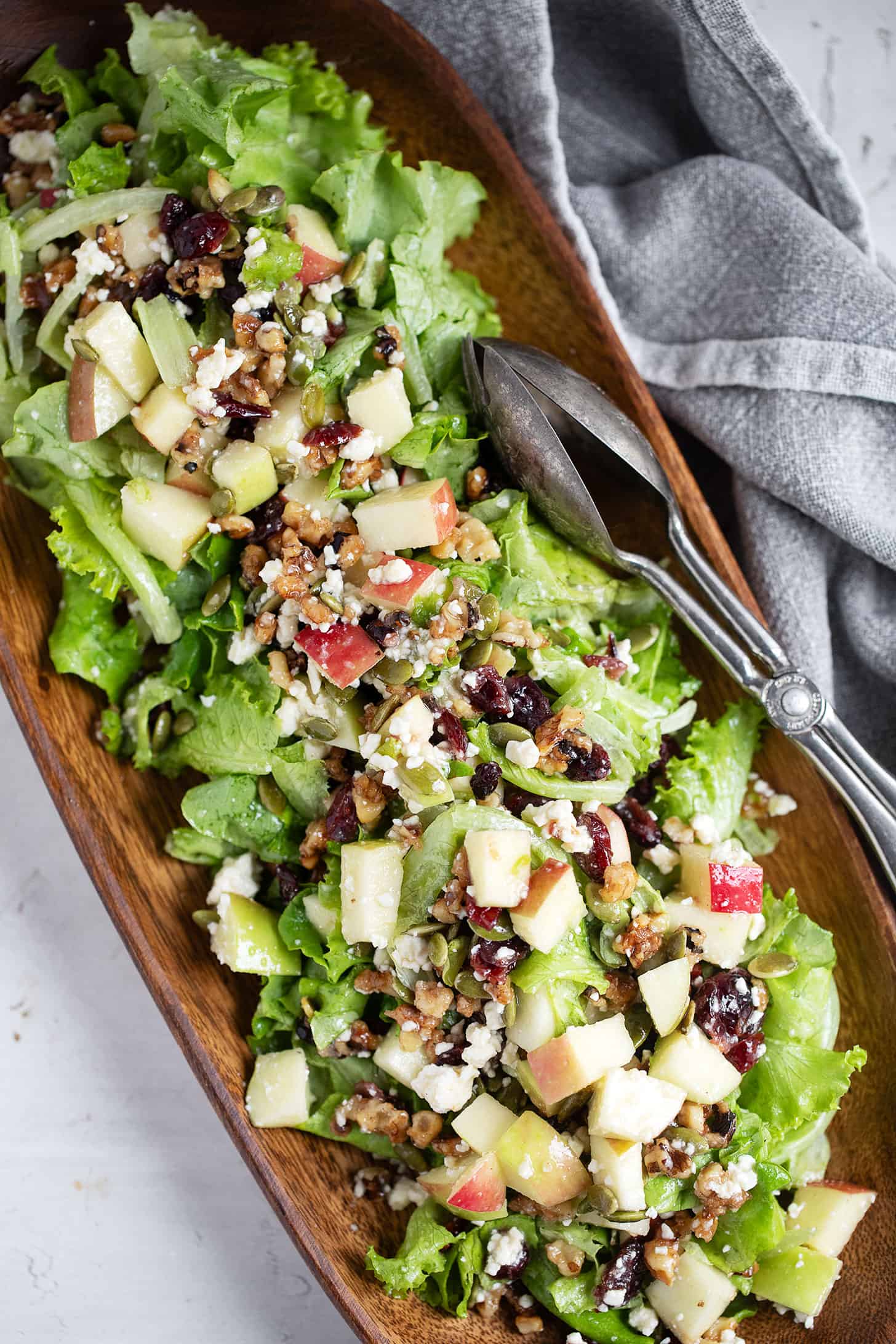 Chopped apple salad in a wooden bowl with silver tongs.