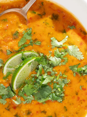 Coconut curry lentil soup in a bowl with cilantro garnish and lime wedges.