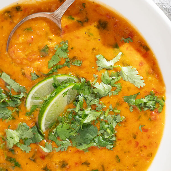 Coconut curry lentil soup in a bowl with cilantro garnish and lime wedges.