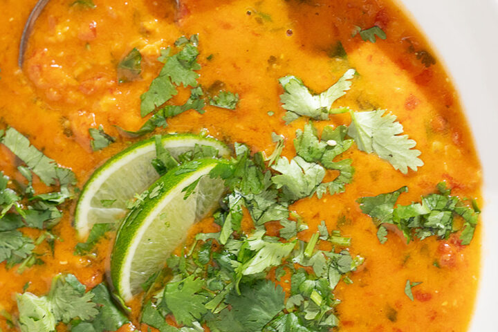 Coconut curry lentil soup in a bowl with cilantro garnish and lime wedges.